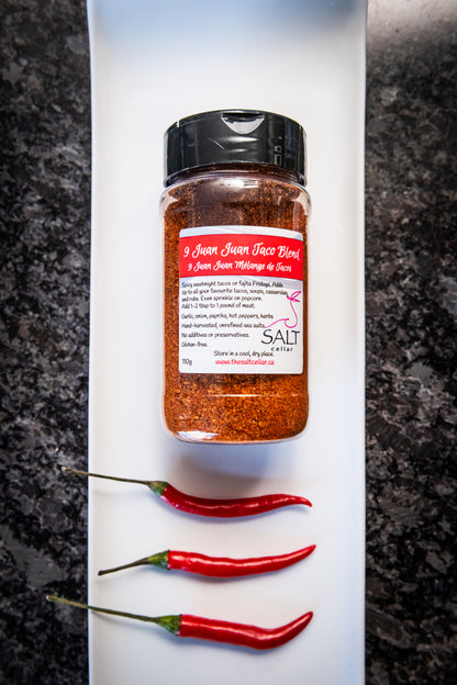 9 Juan Juan Taco Blend seasoning by The Salt Cellar displayed on a white plate with three fresh red chili pepper. This spicy blend, made with garlic, onion, paprika, and hot peppers, is perfect for tacos, avocado toast, popcorn, and more. Gluten-free, no additives, and handcrafted with unrefined sea salt.